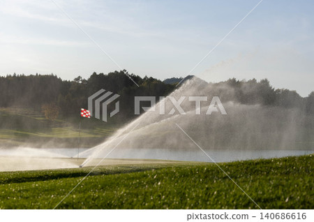 A scene of sprinklers watering the grass on a golf course green. A scene of sprinklers watering the grass on a golf course green. 140686616