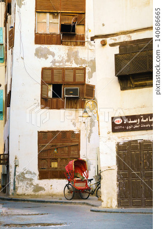 Jeddah, Saudi Arabia- Mar 08 2023, view of the wall of an Arab house with mashrabiya balconies, a red tourist bicycle stroller stands nearby, in the old city of Jeddah, Saudi Arabia Jeddah, Saudi Arabia- Mar 08 2023, view of the wall of an Arab house with mashrabiya balconies, a red tourist bicycle stroller stands nearby, in the old city of Jeddah, Saudi Arabia 140686665