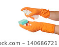 person in orange rubber gloves spraying cleaning liquid from a white spray bottle onto a green sponge 140686721