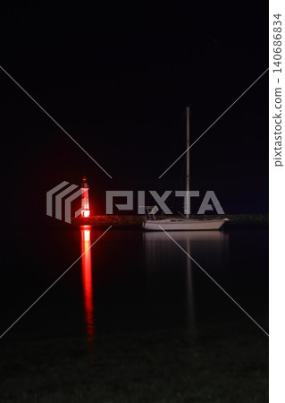 lighthouse and sailboat at dusk. With reflections in the water. lighthouse and sailboat at dusk. With reflections in the water. 140686834