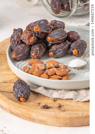 Medjool dates and almonds on a plate with a spoonful of shredded coconut, set on a wooden board with a jar of dates in the background Medjool dates and almonds on a plate with a spoonful of shredded coconut, set on a wooden board with a jar of dates in the background 140687559