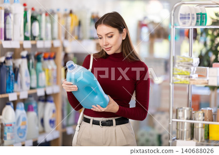 Young woman buyer chooses detergent in store Young woman buyer chooses detergent in store 140688026