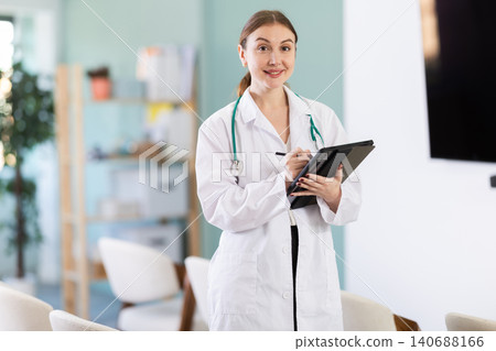 Professional young coach woman doctor standing digital tablet in hands and talking in corporate seminar and inviting in auditorium Professional young coach woman doctor standing digital tablet in hands and talking in corporate seminar and inviting in auditorium 140688166