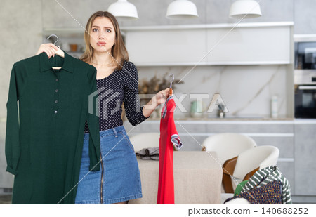 Young upset woman choosing which dress to wear Young upset woman choosing which dress to wear 140688252