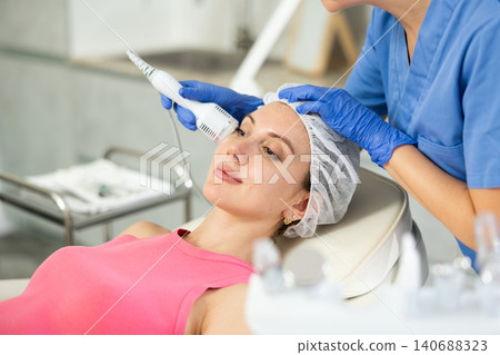 Caucasian brunette girl lying in spa while having facial treatment procedures with modern technologies shrink pores and repair damaged skin. Hardware cosmetology and dermatology Caucasian brunette girl lying in spa while having facial treatment procedures with modern technologies shrink pores and repair damaged skin. Hardware cosmetology and dermatology 140688323