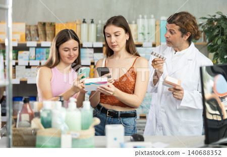 Woman with teen daughter in pharmacy scans QR code on tablets box, pharmacist offer analogue item Woman with teen daughter in pharmacy scans QR code on tablets box, pharmacist offer analogue item 140688352