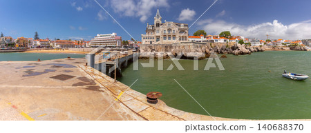 Panoramic view of the Cascais waterfront with a historic coastal mansion, harbor structures and Atlantic coastline on a sunny day in Portugal. 140688370