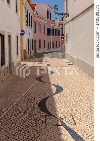 Traditional Portuguese mosaic pavement winds through a narrow historic street lined with pastel buildings in the center of Cascais. Traditional Portuguese mosaic pavement winds through a narrow historic street lined with pastel buildings in the center of Cascais. 140688373