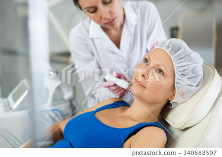 Young female cosmetologist doing microcurrent procedure to adult woman Young female cosmetologist doing microcurrent procedure to adult woman 140688507