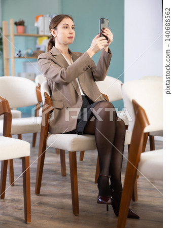 Positive young girl student sitting and listening lecture, taking photo or QR with mobil in lecture hall 140688562