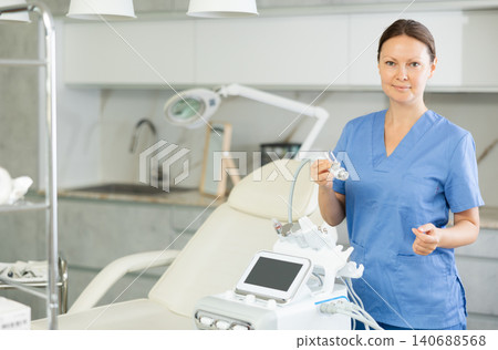 Portrait of cosmetologist standing posing with device for hydrogen oxygen facial beauty machine in medical clinic, looking at camera. Concept of technology hardware for anti age-related changes Portrait of cosmetologist standing posing with device for hydrogen oxygen facial beauty machine in medical clinic, looking at camera. Concept of technology hardware for anti age-related changes 140688568