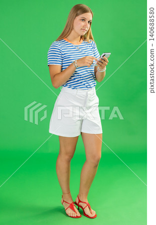 Teenage girl scrolling smartphone in front of green screen Teenage girl scrolling smartphone in front of green screen 140688580