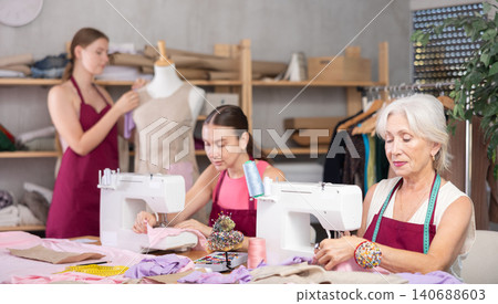 Mature head of manufacturing and female assistant sewing, young designer work with mannequin. Mature head of manufacturing and female assistant sewing, young designer work with mannequin. 140688603