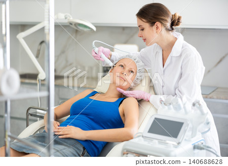 Young doctor doing RF lifting procedure for face lifting of adult woman laying in spa center. Smoothes wrinkles and tightens skin machine Young doctor doing RF lifting procedure for face lifting of adult woman laying in spa center. Smoothes wrinkles and tightens skin machine 140688628