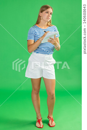 Teenage girl in white shorts takes notes in notebook on green background. Chroma key compositing Teenage girl in white shorts takes notes in notebook on green background. Chroma key compositing 140688643