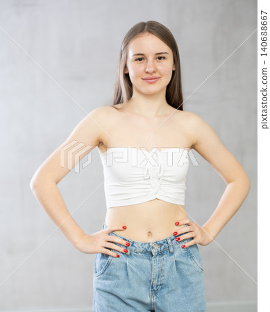 Portrait of young girl in tank top and jeans on gray background Portrait of young girl in tank top and jeans on gray background 140688667