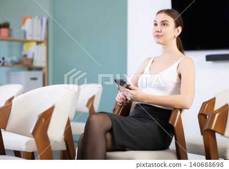Portrait of focused young female student dressed in white blouse and black skirt listening at lesson and writing notes with smartphone in university Portrait of focused young female student dressed in white blouse and black skirt listening at lesson and writing notes with smartphone in university 140688698