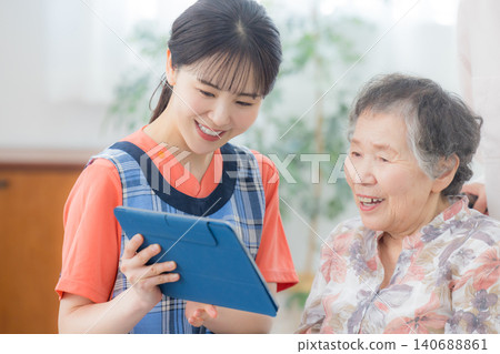 一位護理人員正在使用平板電腦,一位老人坐在輪椅上。 一位護理人員正在使用平板電腦,一位老人坐在輪椅上。 140688861