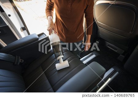 close up hand of woman using portable handheld vacuum cleaner to clean dust on leather car seat of electric car close up hand of woman using portable handheld vacuum cleaner to clean dust on leather car seat of electric car 140689765