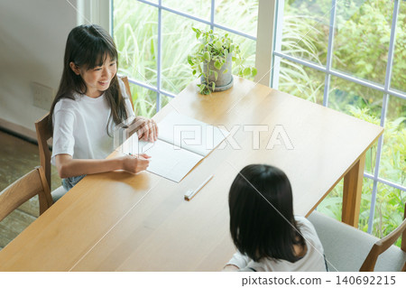 A girl doing her homework and her mother watching over her. A girl doing her homework and her mother watching over her. 140692215
