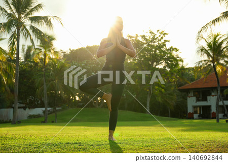 A person does yoga at sunset in Balis palm trees A person does yoga at sunset in Balis palm trees 140692844