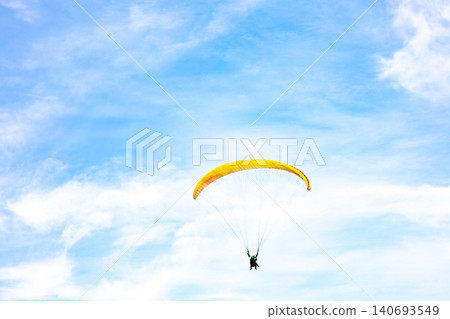 A paraglider flies in the blue sky. 140693549