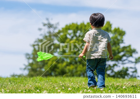 The back view of a boy running across a grassland with a butterfly net in his hand. The back view of a boy running across a grassland with a butterfly net in his hand. 140693611