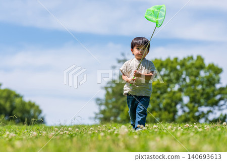 A boy runs across a grassy field under a blue sky, carrying a butterfly net. A boy runs across a grassy field under a blue sky, carrying a butterfly net. 140693613
