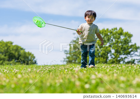 A boy runs across a grassy field under a blue sky, carrying a butterfly net. A boy runs across a grassy field under a blue sky, carrying a butterfly net. 140693614