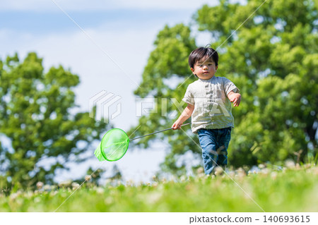 A boy runs across a grassy field under a blue sky, carrying a butterfly net. A boy runs across a grassy field under a blue sky, carrying a butterfly net. 140693615
