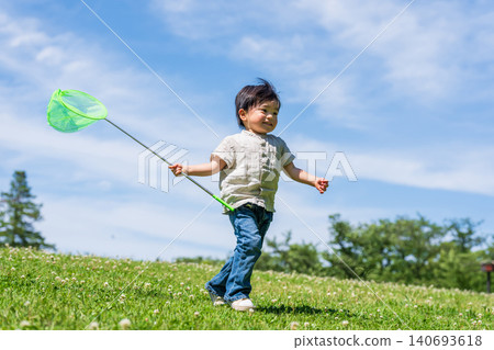 A boy runs across a grassy field under a blue sky, carrying a butterfly net. 140693618