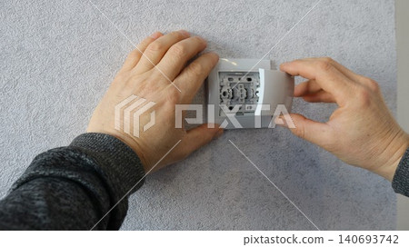 The final stage of installing or replacing a household electrical component, switch, or socket in an interior, the precise moment of assembly of the fittings when the outer part snaps into place The final stage of installing or replacing a household electrical component, switch, or socket in an interior, the precise moment of assembly of the fittings when the outer part snaps into place 140693742