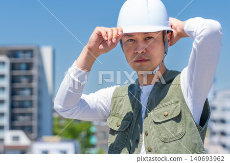 A male worker wearing a helmet under a blue sky A male worker wearing a helmet under a blue sky 140693962