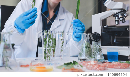 Scientists in lab coats work with plants in a modern lab, focusing on research and experimentation under bright, sterile conditions. Scientists in lab coats work with plants in a modern lab, focusing on research and experimentation under bright, sterile conditions. 140694394