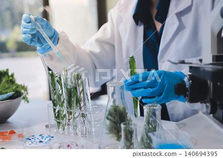 Scientists in lab coats work with plants in a modern lab, focusing on research and experimentation under bright, sterile conditions. Scientists in lab coats work with plants in a modern lab, focusing on research and experimentation under bright, sterile conditions. 140694395