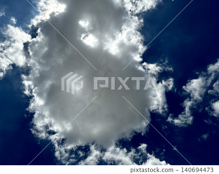 Fluffy white cumulus cloud floating in deep blue sky on bright sunny day with sunlight glowing behind soft cloudscape Fluffy white cumulus cloud floating in deep blue sky on bright sunny day with sunlight glowing behind soft cloudscape 140694473