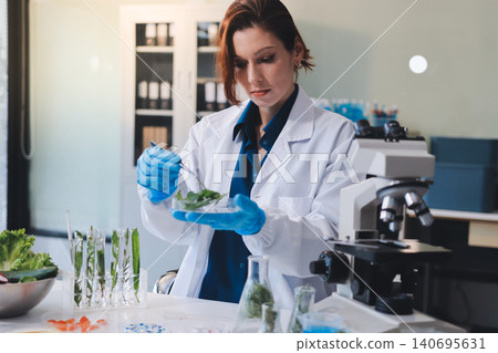 Scientists in lab coats work with plants in a modern lab, focusing on research and experimentation under bright, sterile conditions. Scientists in lab coats work with plants in a modern lab, focusing on research and experimentation under bright, sterile conditions. 140695631