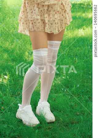 Female legs in transparent white knee-high socks with sneakers on grass during daylight 140695662