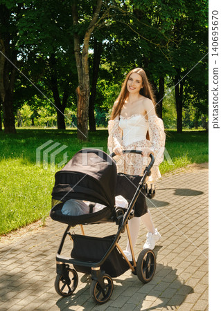 Young mother pushing stroller in park on sunny day with trees along path Young mother pushing stroller in park on sunny day with trees along path 140695670