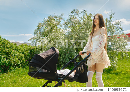Cute mother walks in park with stroller on sunny day surrounded by green trees and grass Cute mother walks in park with stroller on sunny day surrounded by green trees and grass 140695671