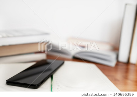Modern black smartphone on a wooden desk next to open books Modern black smartphone on a wooden desk next to open books 140696399