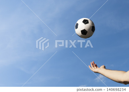 Hand catching a black and white soccer ball against a sky, creating a dynamic scene and soccer background. Hand catching a black and white soccer ball against a sky, creating a dynamic scene and soccer background. 140698234