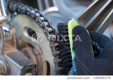 Cleaning motorbike chain with a brush. Close up of a motorcycle service worker cleaning chain of a motorbike, lubricating it with grease Cleaning motorbike chain with a brush. Close up of a motorcycle service worker cleaning chain of a motorbike, lubricating it with grease 140698379