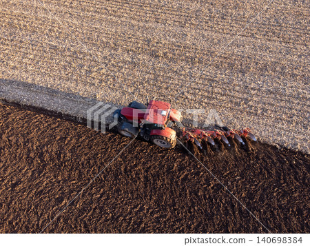 Red tractor working in the field on sunrise. Plowing field in early spring with tractor, concept of agriculture and farming Red tractor working in the field on sunrise. Plowing field in early spring with tractor, concept of agriculture and farming 140698384