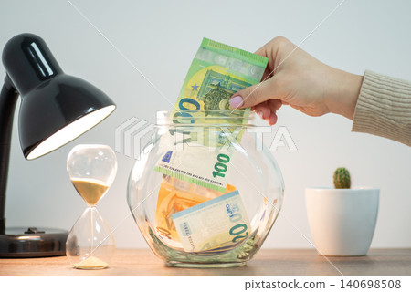 Saving money for a dream. Putting 100 euro banknote to jar, savings concept Saving money for a dream. Putting 100 euro banknote to jar, savings concept 140698508