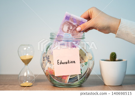 Female hand putting 50 hryvnia banknote to glass jar with inscription education. Saving up money for education in Ukraine 140698515