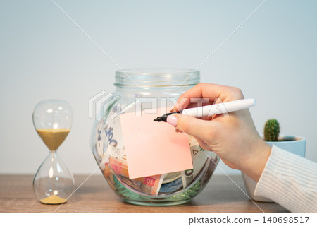 Saving up money in Ukraine. Jar with hryvnia money and blank paper, writing inscription with marker Saving up money in Ukraine. Jar with hryvnia money and blank paper, writing inscription with marker 140698517