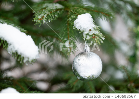 Silver ball on the of branch of fir tree covered with snow, close up. Christmas decoration outdoors, festive mood, charmy and magical atmosphere in garden Silver ball on the of branch of fir tree covered with snow, close up. Christmas decoration outdoors, festive mood, charmy and magical atmosphere in garden 140698567