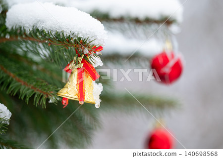 Close up shot of Christmas toys on the fir tree branches, covered with snow. Outdoor decoration for winter holidays, festive atmosphere in the yard Close up shot of Christmas toys on the fir tree branches, covered with snow. Outdoor decoration for winter holidays, festive atmosphere in the yard 140698568