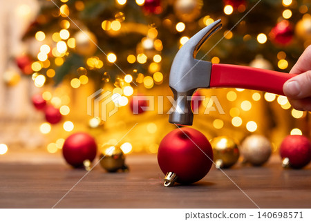 Hammer in male hand above the red christmas ball, going to break it, close up. Christmas decoration, lack of christmas mood, end of winter holidays concept Hammer in male hand above the red christmas ball, going to break it, close up. Christmas decoration, lack of christmas mood, end of winter holidays concept 140698571